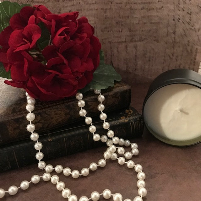 Flower bouquet laying on top of books and a string of pearls with a candle next to it